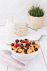 Served breakfast table. White bowl of fresh muesli with colorful berry fruits, on top of white wooden breakfast table.