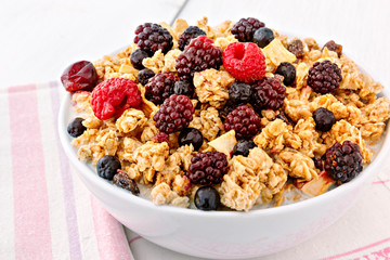 Bowl of muesli with colorful berry fruits, on top of white wooden table.