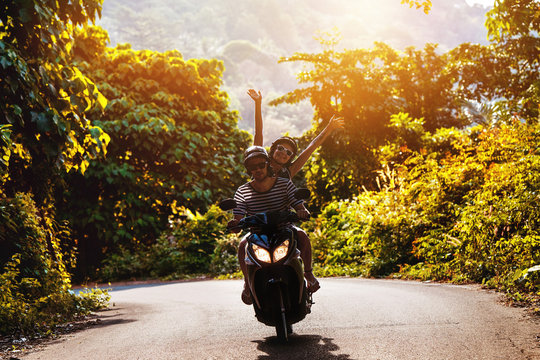 Happy couple on scooter against sunset tropic road