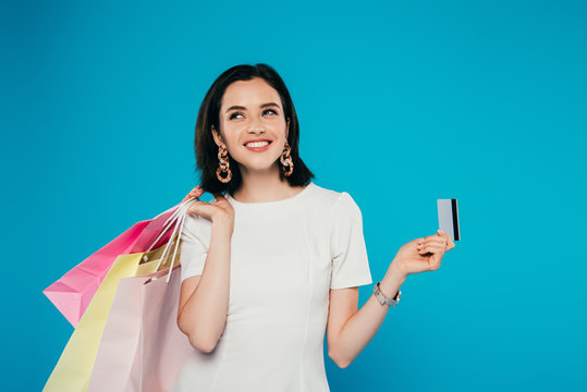 smiling elegant woman in dress with shopping bags holding credit card isolated on blue