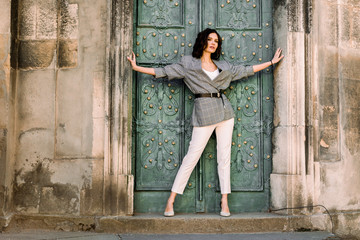 A young woman in white pants and checkered jacket with dark hair stands and looks into the distance...