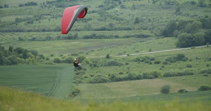 Person flying on paraplane above beautiful green rural meadow, active lifestyle, activity