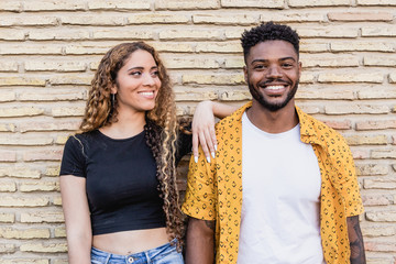 Portrait of a young interracial couple smiling on a brick wall