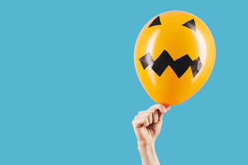 Hand of person with bright orange balloon with black stickers looking like scary face for Halloween decoration