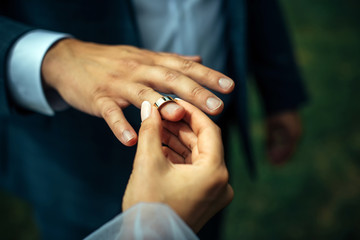 Young bride put a gold wedding ring on the groom's finger, close-up. Wedding ceremony, exchange of rings.