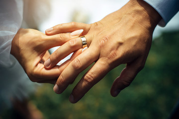 Young bride put a gold wedding ring on the groom's finger, close-up. Wedding ceremony, exchange of...