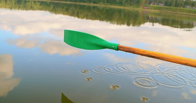 Rowing boat ride on a calm lake. Blue sky and white clouds reflected in the water. Water with green algae and reeds. Drops of water dripping from the oars. Beautiful patterns on water. Romantic trip.