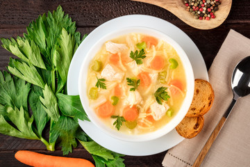 Chicken noodle soup close-up with ingredients on a dark rustic wooden background