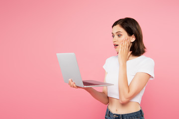 Fototapeta premium shocked pretty girl using laptop isolated on pink