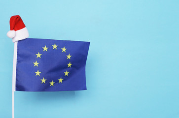 Flag of European Union with little santa claus hat on blue background. New Year winter holiday concept, copy space