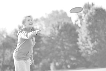 Black and white photo of Smiling and healthy senior woman catching disc in park