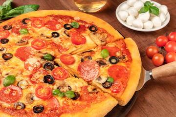 Pepperoni pizza with salami slices, black olives, mushrooms, fresh basil leaves and a lot of cheese, on a dark rustic wooden background