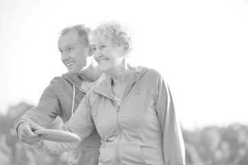 Black and white photo of Loving active couple throwing flying disc together in park
