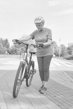 Black and white photo of Active senior woman walking with bicycle in park