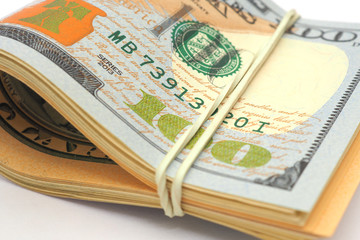 A rolled up bundle of dollars lies on a white paper background. Above is a 100 dollar bill of a new...