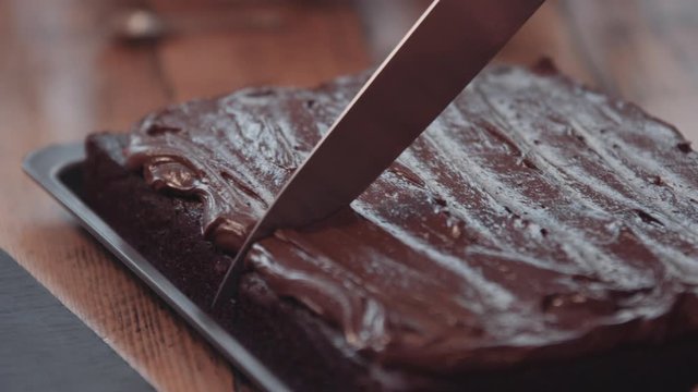 Baker slicing fresh chocolate brownies with knife 