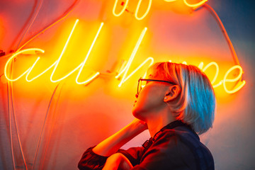 Young adult asian female wearing glasses in front of neon light sign, shallow selective focus