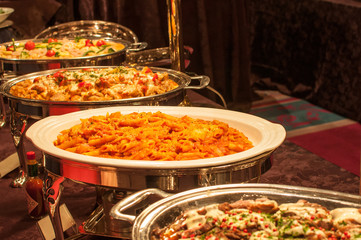 Penne with tomato sauce, roast chicken, and other food served in chafing dishes at a buffet party