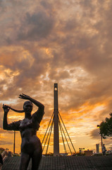 Sunset with a silhouette of a bronze statue of a woman, and a concrete tower