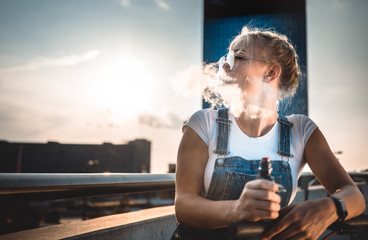 Woman smoking electronic cigarette outdoor on modern city buildings background