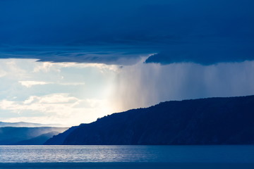 Storm with heavy rain and bright sun over the shore of lake Baikal