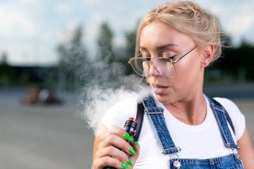 Portrait of young woman vape an electronic cigarette outdoor