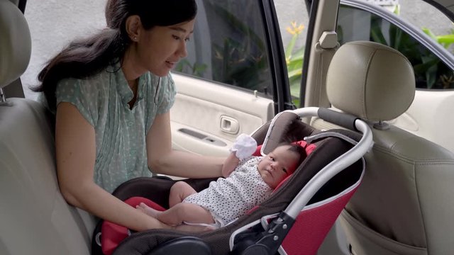 asian young mother putting her daughter in car seat when prepare to go