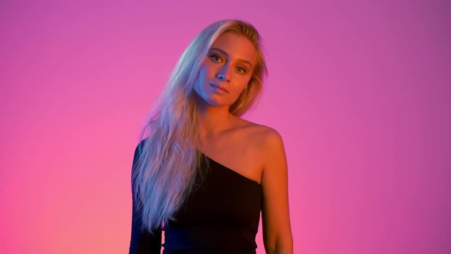 Indecisive pretty young woman with unsure face shrugs and spreads her hands thinking of problem solution in neon vivid lights red and blue
