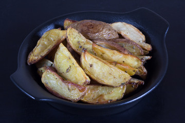 Close up rustic roasted potatoes on black plate on black background