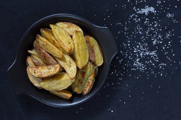 Top view of rustic roasted potatoes with rosemary branch on black plate on black background
