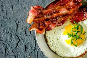 Fried bacon and egg on skillet From above appetizing breakfast with egg and bacon on steel frying pan against textured gray background