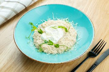 Breakfast. Oatmeal with parmesan and poached egg in a blue bowl on a wooden background. Close up, selective focus