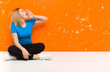 young blonde woman yelling loudly and angrily to copy space on the side, with hand next to mouth...