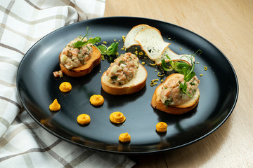 Salmon tartare on fried croutons served on a stylish black plate. Restaurant Food. Wooden bakcground. Close up