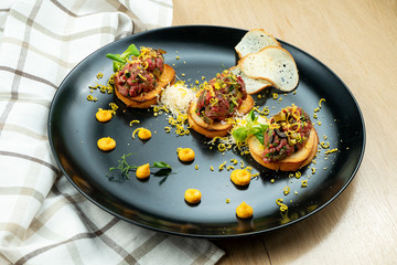Beef tartare on fried croutons served on a stylish black plate. Restaurant Food. Wooden bakcground. Close up