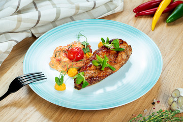 Grilled chicken fillet with tomato salsa served on a blue plate on wooden background. Restaurant serving. Close up. Selective focus