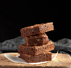 stack of baked square pieces of chocolate brownie cake on brown wooden cutting board
