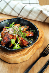 Grilled chicken wings in honey and beer sauce served in a decorative pan with herbs. Close up, selective focus. Wooden background. Food photo