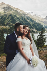 Beautiful wedding photo on mountain lake. Happy Asian couple in love, bride in white dress and...