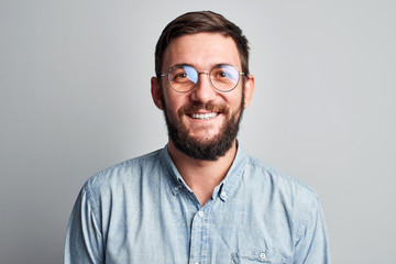 Friendly face portrait of an authentic caucasian bearded man with glasses of toothy smiling dressed casual against a white wall isolated - obrazy, fototapety, plakaty