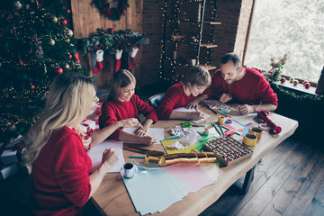 Photo of big four members family parents and two children spending x-mas morning together parents assist in writing santa letter sitting table indoors wear red jumpers