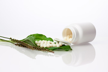 Bottle with homeopathic pills on green plant leaf. Homeopathy, naturopathy and alternative herbal...