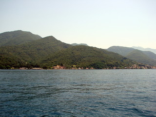 The beauty of the Montenegrin hills is covered with dense green forest reflected on the water surface of the azure bay.