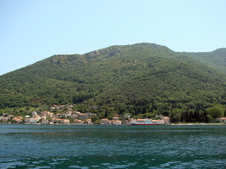 Fototapeta na wymiar Landscape from the sea of ​​small Montenegrin seaside settlements near the azure bay surrounded by hills covered with dense green forest.