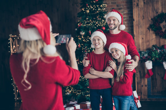 Photo of mom making photo of two children and daddy near decorated garland newyear tree indoors family x-mas atmosphere wear santa caps and red sweaters