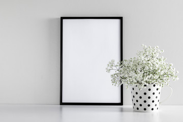 Black frame photo on white wood table and small white flowers in vase. White gypsophila flowers on...