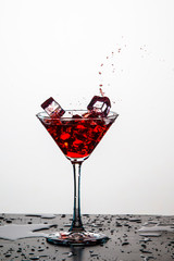 Action Splash Photography. Red Wine Glass With Splashes Against White Background. Vertical Image Composition