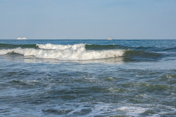 The sea is worry, waves with foam. The white ships on the horizon.