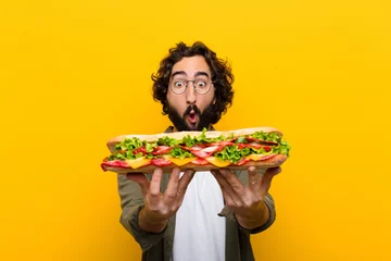 Selbstklebende Fototapeten junger verrückter bärtiger Mann mit einem riesigen Sandwich. © kues1