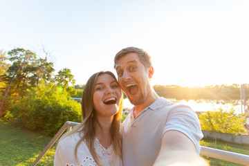 Beautiful funny romantic couple on nature background. Attractive young woman and handsome man are making selfie, smiling and looking at camera.